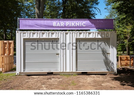 White modular container used as a bar and picnic store with a purple banner on top of it