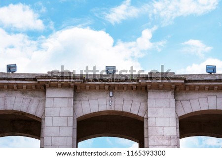 Stone arch with searchlights against the background of the blue sky. Fullface