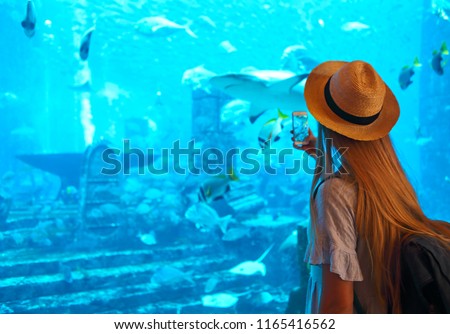 Sillouette of the woman in hat taking picture in large aquarium in Dubai