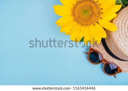 Fashion flatlay with sunglasses, straw boater hat and bright big yellow sunflower on blue background. Flatlay style.