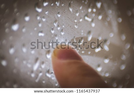 Moody Feelings Concept: Finger Of A Teenager Drawing On The Window With Raindrops On A Rainy Day