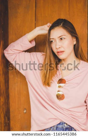 A woman wearing a pink shirt standing against a wooden door.