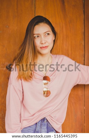 A woman wearing a pink shirt standing against a wooden door.