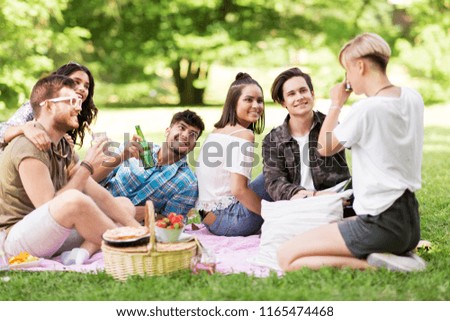 friendship, leisure and technology concept - group of happy smiling friends with non alcoholic drinks photographing at picnic in summer park