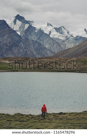 Traveller man in red jacket standing on meadow with lake and snow mountain view. Travel lifestyle, adventure and success concept