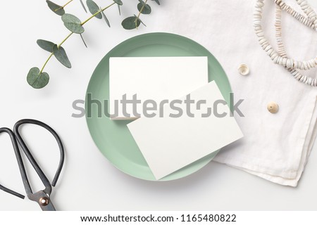 stack of blank business cards on a white feminine styled desk with mint bowl, decorative scissors, linen napkin and eucalyptus twigs. minimalist mock up, flat lay / top view