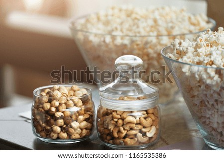 Glass bowls with popcorn and jars with nuts on table