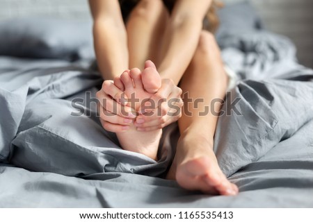 Young woman massaging her foot while sitting on bed Royalty-Free Stock Photo #1165535413