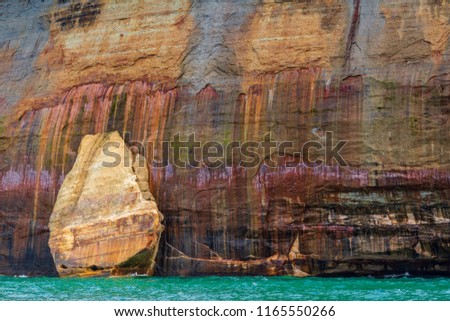 A mitten shaped rocks against the a stone cliff at Pictured Rocks National Lakeshore in Northern Michigan. These mineral laden cliffs have a painted look in the sandstone rock formations