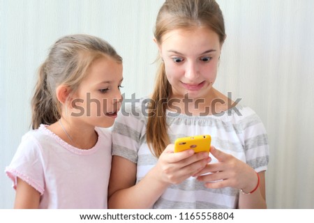 Two girl with pony tail hair, play game on smartphone, smiling and make funny faces
