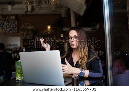 Woman wearing in glasses having video conference via laptop computer while sitting in restaurant interior. Female manager having online call via notebook device. Webinar via netbook 