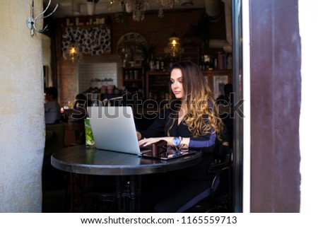Beautiful female skilled publication specialist typing text on laptop computer  while sitting in restaurant interior. Charming woman working on notebook device during free time in coffee shop. 