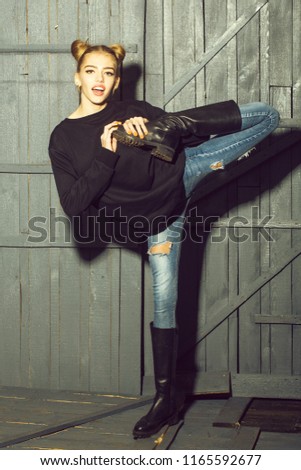 Full length view of one straight slender funny young smiling happy woman with cool hairstyle in torn jeans and black sweater with flexible body standing in studio on wooden backdrop, vertical picture