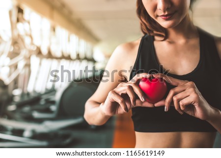 Happy sport woman holding red heart in fitness gym club. Medical cadio heart strength training lifestyle. Pretty female sport girl workout exercise. Cardiac healthy and wellbeing. Massage ball in hand Royalty-Free Stock Photo #1165619149