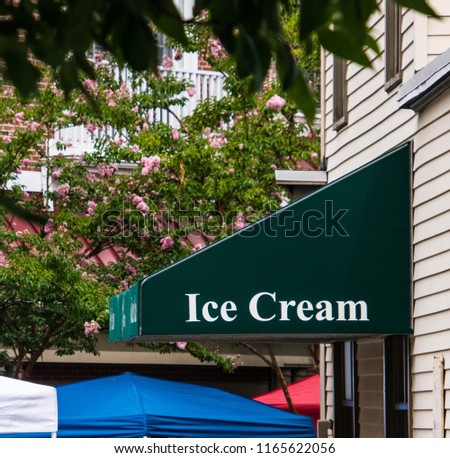 Dark green awning over store entrance on a yellow sided building. There are portions of large white, blue and red umbrellas visible. Awning says Ice Cream on it