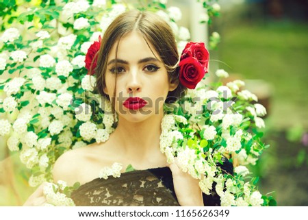 woman with fashionable makeup and red lips, has rose flower in hair hispanic or spanish style in black dress at white spring or summer blossom on natural background