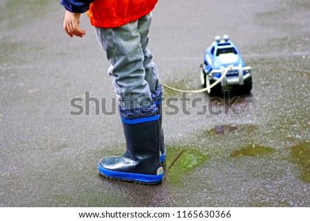 Children walk in autumn. The boy walks in puddles. In the hands of the child the rope from the toy car.