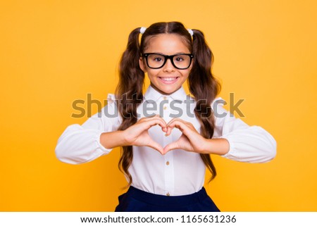 Portrait of cheerful, joyful, nice, lovely, sweet small brunette girl isolated on yellow background makes heart with her hands