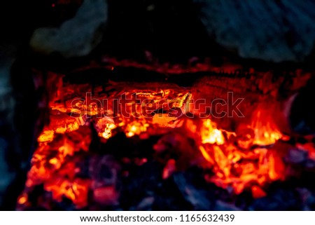 Red hot glowing embers in a wood stove surrounded by shadowed dark wood. The area looks like a glowing cave.