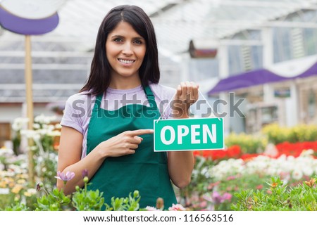 Woman in garden center pointing at the open-sign while smiling