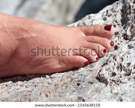 female foot with nails with red enamel on a marine rock