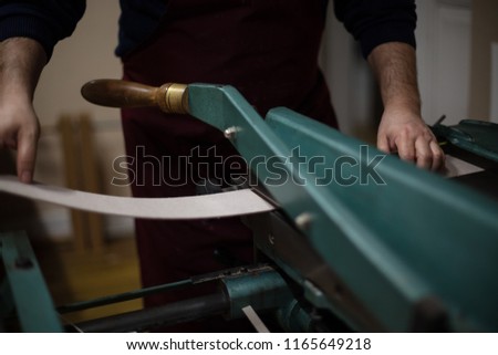 Man cutting paper and card on a large guillotine on a work table in a book binders workshop in a close up view