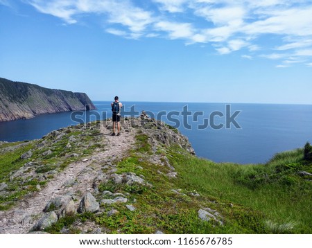 Man taking a photo on his camera of the open and calm atlantic ocean along the sugarloaf trail in Newfoundland and Labrador, Canada