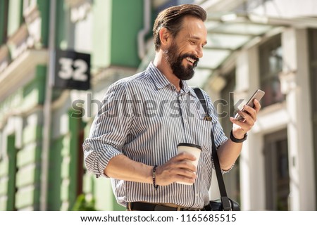 On my way to work. Waist up of cheerful bearded man using his smartphone and drinking coffee Royalty-Free Stock Photo #1165685515