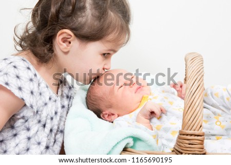 young child girl sister kiss brother boy newborn baby lying in basket