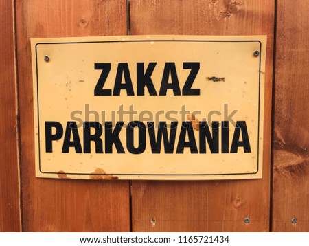 „Zakaz parkowania” which means „No parking” in Polish. Yellow sign on wooden fence