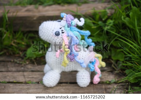 Crocheted toy on old wooden stairs outdoors. White unicorn with colorul mane.