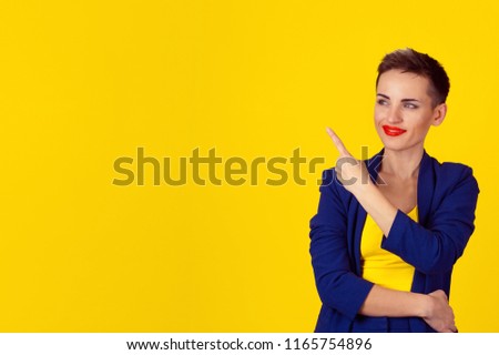 Closeup portrait young happy smiling woman presenting with index finger pointing to copyspace, looking to side up isolated on yellow background. Positive human emotion, facial expression feeling sign