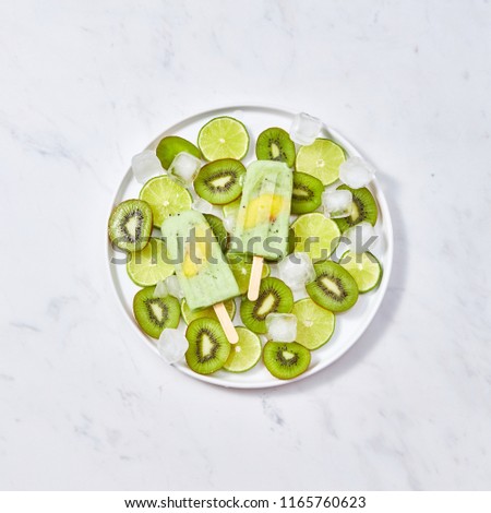 Dietary, healthy fruit frozen smoothies with a piece of peach on a stick in a plate with pieces of kiwi, lime and ice cubes on a gray marble table with a copy of the space for text. Flat lay