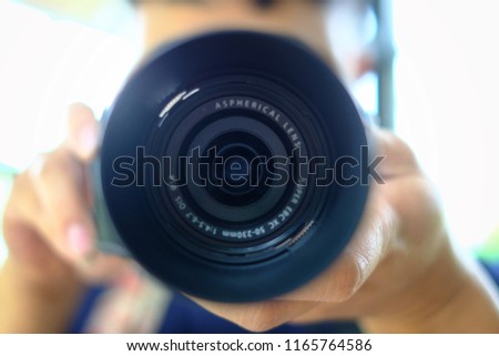 Man photography in navy blue T-shirt holding black camera and take a photo with green burred background.