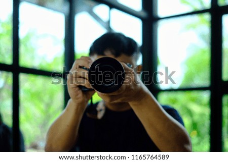 Man photography in navy blue T-shirt holding black camera and take a photo with green burred background.