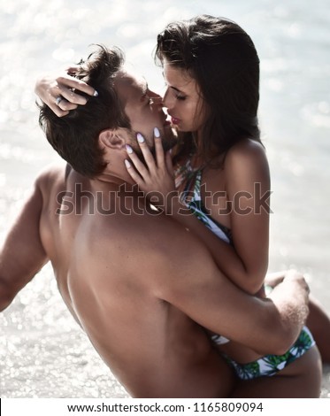 Happy cheerful couple kissing hugging in the sea together with splashes of water on a tropical beach at sunset. Romantic vacation, honeymoon love