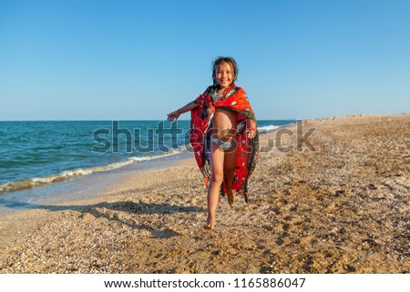 Happy smiling little girl playing with an inflatable ball on the beach by the sea shore in summer