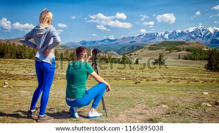 Travel photographer taking nature photo of mountain landscape. Hiker tourist professional man with woman on adventure vacation shooting slr camera on tripod.