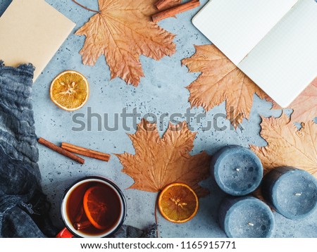Autumn frame flat lay composition on a grey concrete background. Maple leaves, season tea,   open notebook with empty sheets, black aromatic candles and warm scarf.
