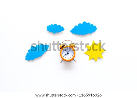Time of day. Morning. Awakening and sunrise. Sun and clouds cutout near alarm clock on white background top view space for text