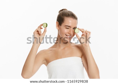 Young beautiful, happy woman is holding some cucumber in front of her smiling face. Isolated over white background.
