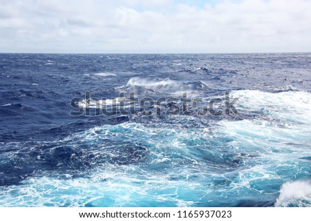 Storm waves in the world ocean. Kind of waves, crests, splashes, foam against the background of the sea horizon and the blue sky and clouds. A view of storm waves from the ship's side.