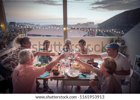group of different ages people in friendship eat together a dinner event cheering with wine and enjoy the lifestyle. happiness and joyful for friends at home in the terrace with houses and ocean view