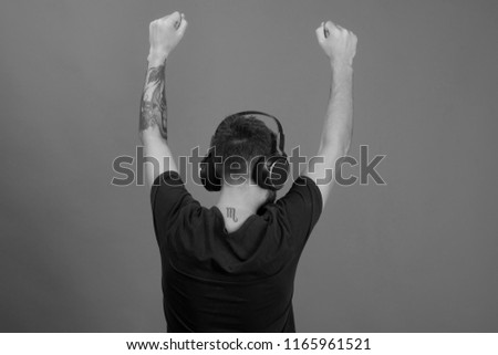 Man holds hands up, dancing turned around on blue background. Relax and music concept. Singer enjoys music partying. Dj with scorpio tattoo wears headphones, copy space.