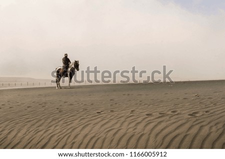 Horseman ride his horse at desert with white clouds background.