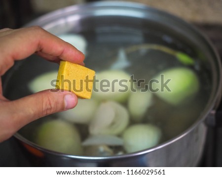Bouillon, stock or broth cubes in female hand with a pot of soup. Broth made by stewing maet, fish in water.