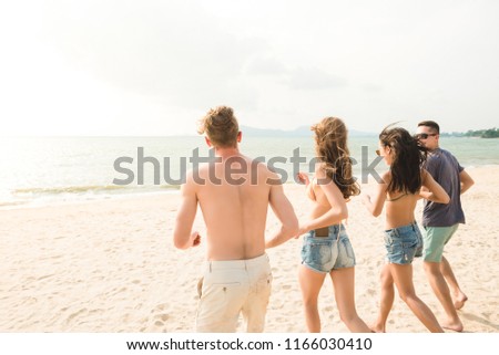 Group of young happy friends running from the beach to the sea, having fun during summer vacations