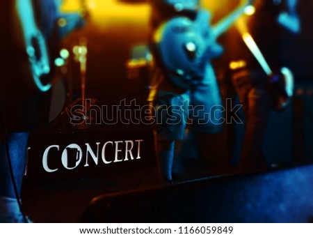 A rock band in front of a neon sign that says concert. The o is a pitcher.