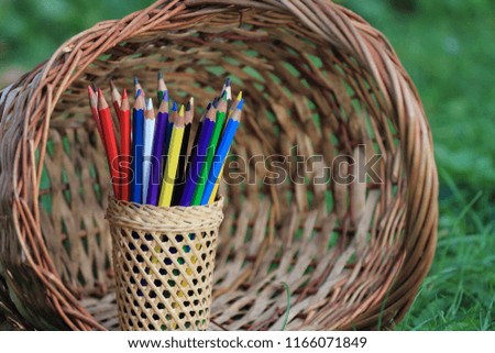 Colored pencils with a basket of knowledge on the grass.