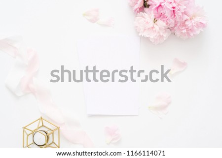 Delicate feminine wedding or birthday flat lay composition with peonies floral bouquet and candle. Blank paper card, mockup, invitations. Flatlay, top view.